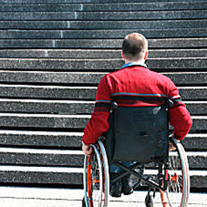 Mann im Rollstuhl, der vor einer Treppe steht und nicht weiter kommt.