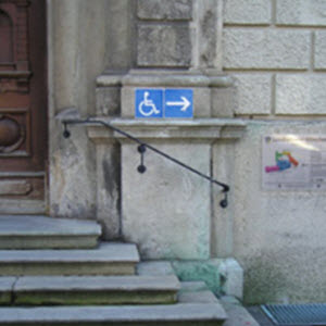 Eine Treppe mit einem Schild, dass der Behinderten-Eingang auf der Rückseite ist.